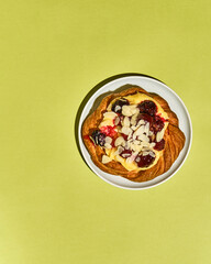 Sweet pastries, a bun with raspberries, almonds and cream on a plate on a colored background in a modern style, top view with space for text