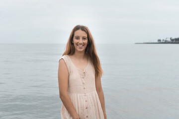 Happy Hispanic female in a beige sundress posing in the sea background