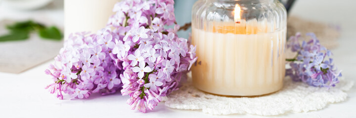 Beautiful composition with fresh violet lilac bouquet in watering and candles. Cozy atmosphere. Greeting card for Saint Valentine's Day, 8 march, Women's day, Mother's day. White background banner