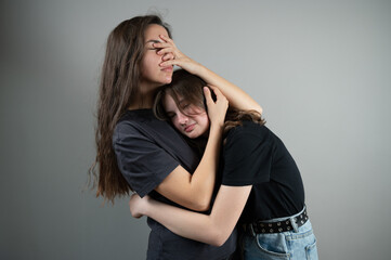 Concept of family support and trust. Mom hugs and comforts teenage daughter on gray background