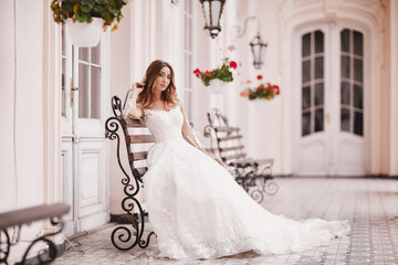 Beautiful bride is sitting on wooden bench in old city. young woman with long hair in lace satin wedding dress in ancient town. Smile and love. wedding day