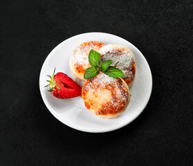 Three cheesecakes on a white plate with powdered sugar with a slice of strawberries on a black background.