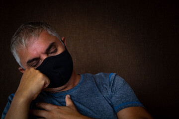 Obraz premium Middle-aged man with white hair and face mask in times of pandemic. With her head resting on his hand.