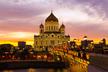 Fototapeta na wymiar Orange sunset in Moscow: the view of the Cathedral of Christ the Savior and the pedestrian Patriarshy Bridge.