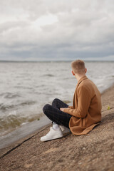 Fototapeta na wymiar Young guy sits on the seashore.