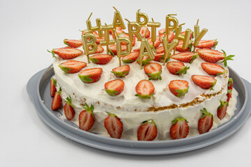 Close-up of isolated strawberry cheesecake on white background decorates with golden candles as happy birthday letters.