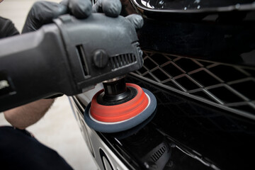hand with a polishing tool cleaning a bumper on a black car