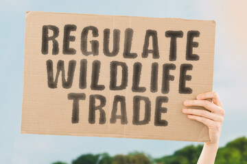 The phrase " Regulate wildlife trade " on a banner in men's hand. Human holds a cardboard with an inscription. Warning. Illegal. Legislation. Rules. Policy. Regulations. Catch. Killing. Animals - Powered by Adobe