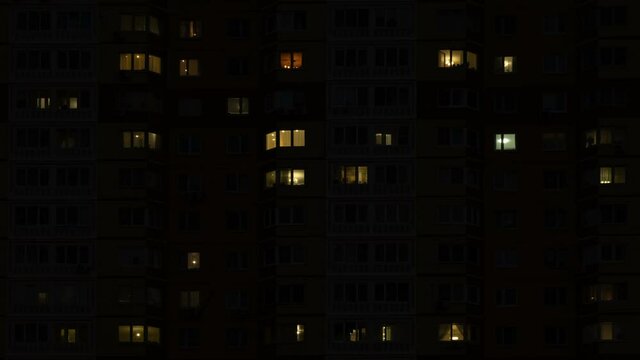 Time lapse of lights turning on and off in windows of residential apartment building at night.