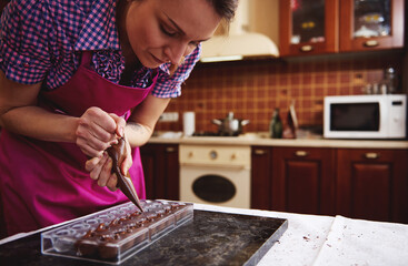 Chef pastry squeezing sweet creamy liquid from confectionery bag into candy molds for making luxury...