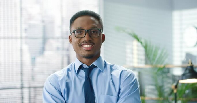 Close up portrait of young handsome male office worker looking at camera with smile on face. Close up portrait of African American businessman in cabinet at workplace, business concept