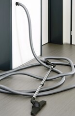 Long central vacuum cleaner hose laid on the grey floor in the room. Hose of central vacuum cleaner plugged into a wall inlet valve socket. - obrazy, fototapety, plakaty