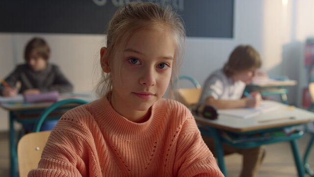 Serious Student Posing At Camera In Classroom. Cheerful Girl Sitting At Desk 