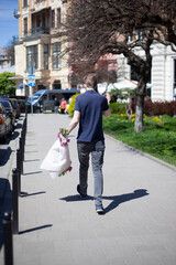 A young man with a large bouquet of flowers walks down the street