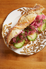 Top view of a thai chicken sandwich served on an white ornate plate with gold details on a wooden surface