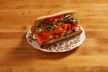 Smoked carrot sandwich served on an white ornate plate with gold details on a wooden surface