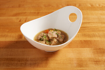 Chicken and vegetable soup served in a white bowl on a wooden surface