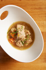 Top view of chicken and vegetable soup served in a white bowl on a wooden surface