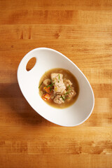 Top view of chicken and vegetable soup served in a white bowl on a wooden surface