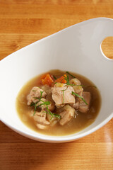 Chicken and vegetable soup served in a white bowl on a wooden surface