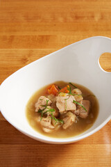 Chicken and vegetable soup served in a white bowl on a wooden surface
