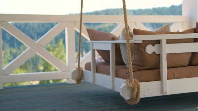 Close up of lightly swinging on summer wind comfortable couch swing on open outdoor terrace at suburban house.