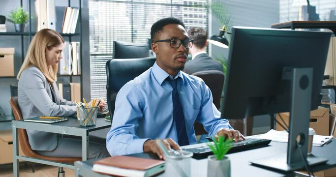 Portrait of young busy African American male worker in office typing on computer, looking at monitor with concentrated face, handsome businessman, office people working in cabinet, business concept