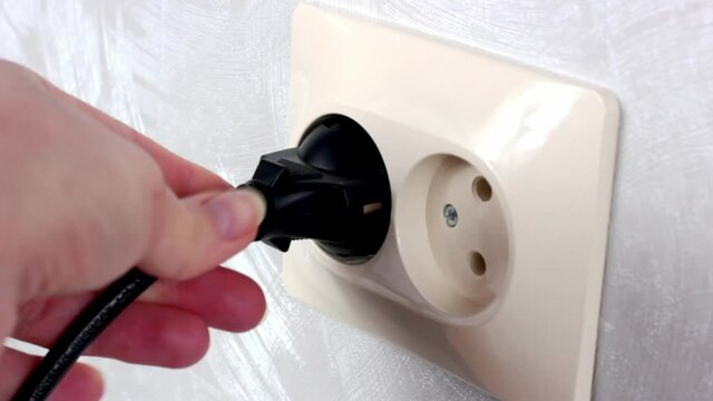 Caucasian woman hands switch on the black power plug into the white electrical socket close up