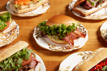An assortment of sandwiches featuring BLT sandwich served on an white ornate plate with gold details on a wooden surface