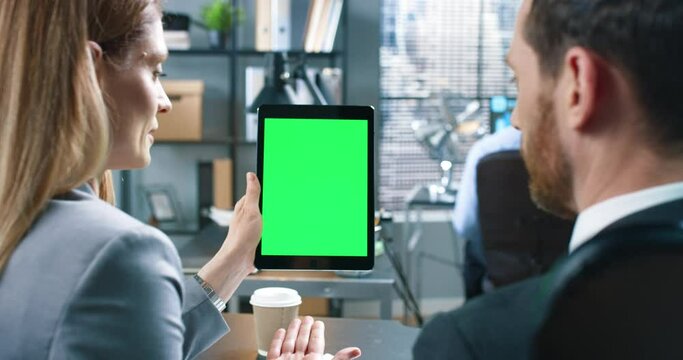 Rear of Caucasian businesswoman holding in hand tablet with chroma key and chatting with young male boss at office cabinet looking at device with green screen, business. Close up concept