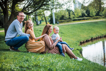 Fototapeta na wymiar happy family on the bank near the river in summer in the park. Concept of family vacation in nature. dad and kids, father's day