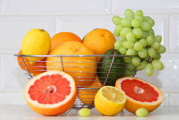 Fruits in a vase oranges grapefruits, tangerines, lemons, avocados, grapes and next to it is a cut grapefruit and lemon. lemon and red grapefruit in the cut