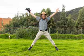 young man photographer and traveler jumping in nature holding camera in his left hand with hands and legs stretched out and smiling.