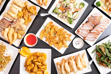 Crab rangoon, lemon chicken, pork spare ribs, tempura shrimp. Asian food for dinner on a table. Chinese food spread.