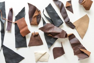 various black, brown, tan, and red-brown leather pieces scattered on a white ground - photographed...