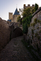 Fototapeta na wymiar Medieval castle towers stand out in the background over the stone walls of an cobbled alley in the Cite of the fortified city of Carcassonne at sunrise, UNESCO World Heritage Site, France