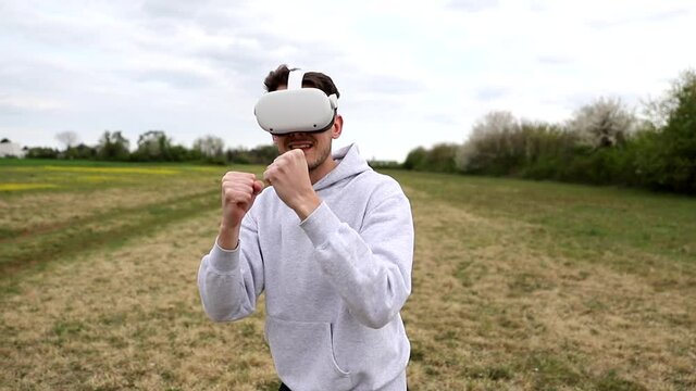 A boy in an open-air meadow plays a boxing game using virtual reality headsets.