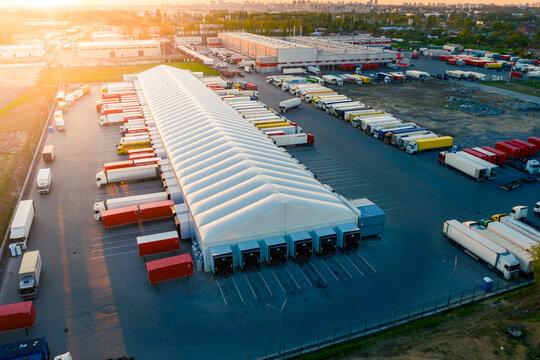 Logistics park with warehouse and loading hub. Semi-trailers trucks stand at ramps and wait for load and unload goods. Aerial view at sunset