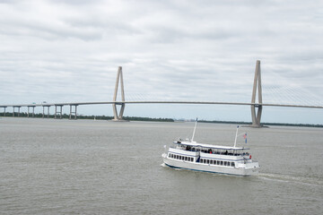 Fototapeta premium A tour boat on the the Cooper River in front of the Ravenel Bridge in Charleston, South Carolina during a cloudy day