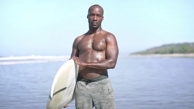 Young attractive surfer guy with surfboard, fit african american black man.  tropical island beach. Concept of Fitness Healthy Active Living, Surfing. Summer Vacation. Slow motion. 