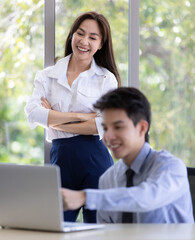 Beautiful black long hair Asian businesswoman and gook looking cute Asian businessman working together in office with intimate gesture and teamwork pose. They smile and laugh together