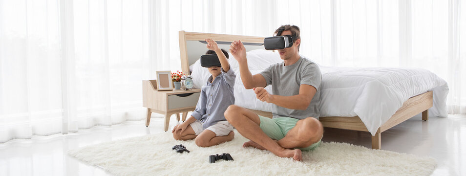 Father and his mixed-race son wearing vr virtual reality device to play a game together with fun and happy in bedroo