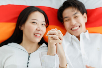 LGBTQ couple lovers, a handsome girl as a man or butch femme laying and hold hands on LGBT symbol flag. spending and sharing loving time with fun, warmth, and happiness. Selective focus on hands