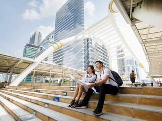 Wide-angle portrait of cute smiling young Asian lover tourists sitting and holding the paper map on...