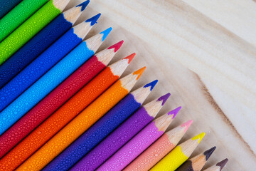 Multicolored pencils with water drops on wooden table, top view, selective focus