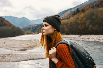 beautiful woman in a sweater with a backpack travels near a mountain river in nature side view