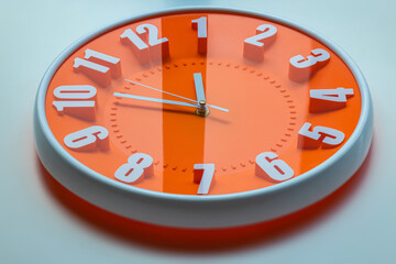 Obraz na płótnie Canvas Orange clock face of a wall clock show the time. It's close to 12 o'clock. The latest report of the atomic scientist shows the doomsday clock 100 seconds to twelve. Time is running out for mankind.