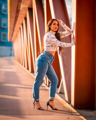A brunette Latin girl in jeans in the city at sunset. Perched next to the orange bridge