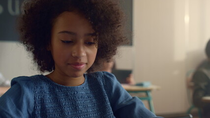 Cheerful african american girl sitting at desk with tablet computer in school