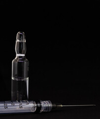 A crystal ampule and a syringe with needle on dark black background. Medicine and pharmaceutical...